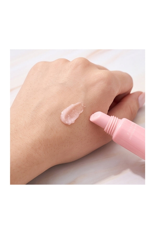 A close-up of a hand showing a swatch of pale pink cream or balm, with a pink tube applicator touching the product on a light marble-like surface.