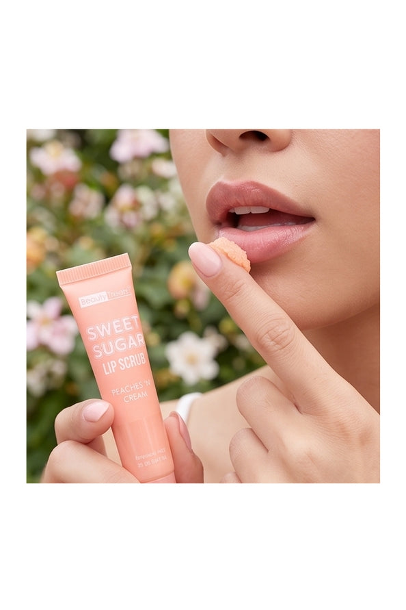 A close-up of a person holding a peach-colored tube of Sweet Sugar Lip Scrub and touching their lips, with a soft-focus background of flowers.