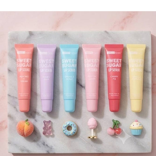 Six lip care tubes from the brand 'Sweet Sugar' arranged in a row on a white marble tray. The tubes are peach, lavender, light blue, pink, red, and yellow, with small decorative food props placed below them on a pink marble background.