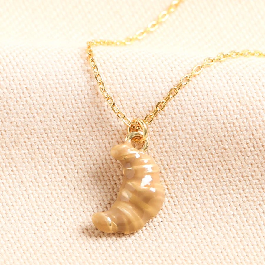 Gold necklace with a ceramic croissant pendant on a light pink fabric background